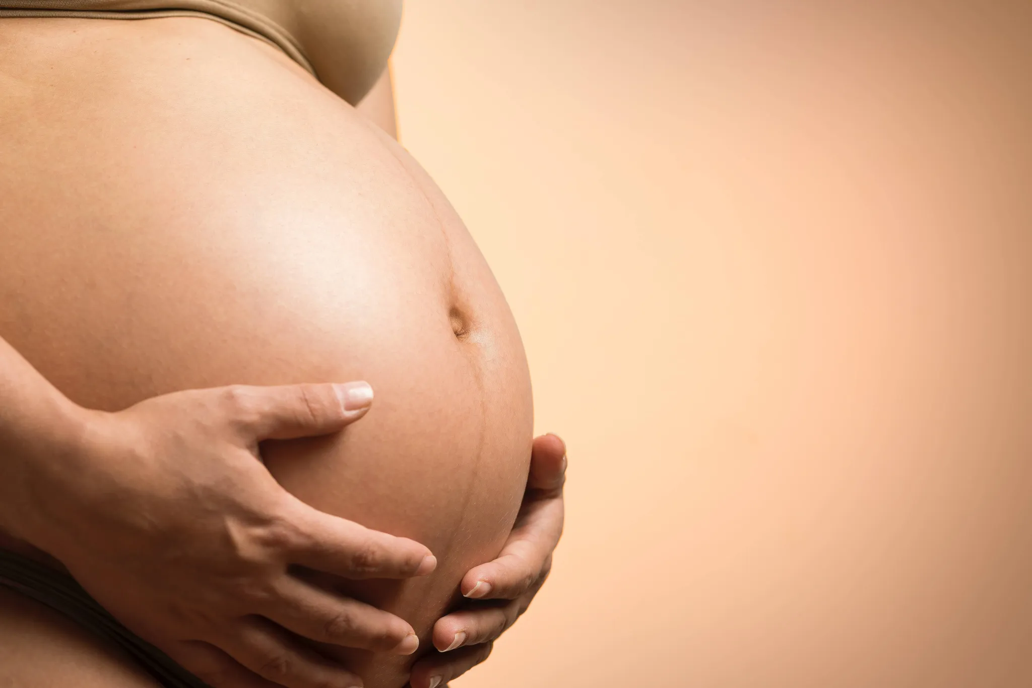 Eine Schwangere hält ihren Babybauch mit beiden Händen.